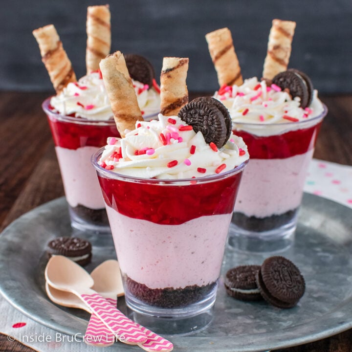 Three clear cups filled with strawberry cheesecake, cookie crumbs, and pie filling.