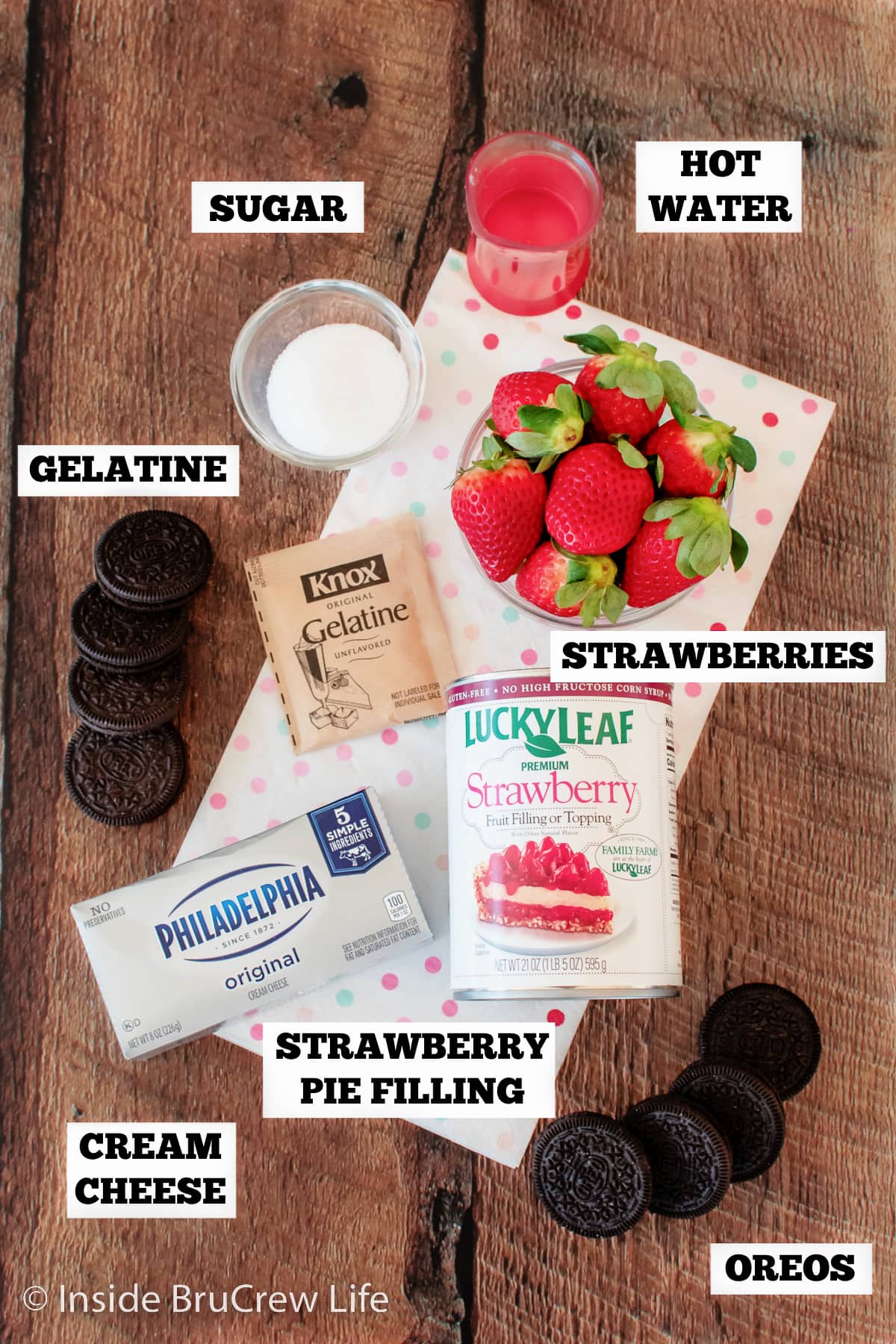 A brown board with bowls of ingredients to make strawberry parfaits.