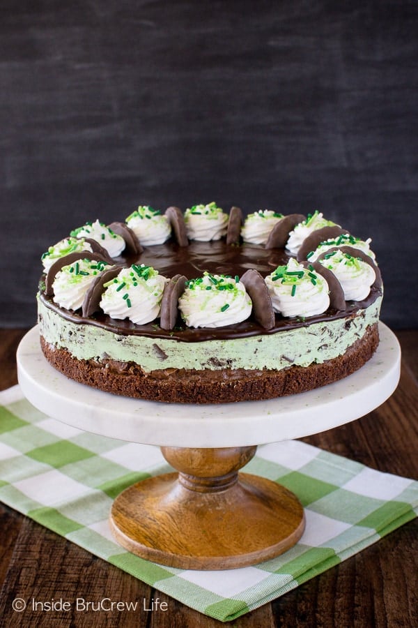 A white cake stand with a mint cheesecake on a brownie crust on it.
