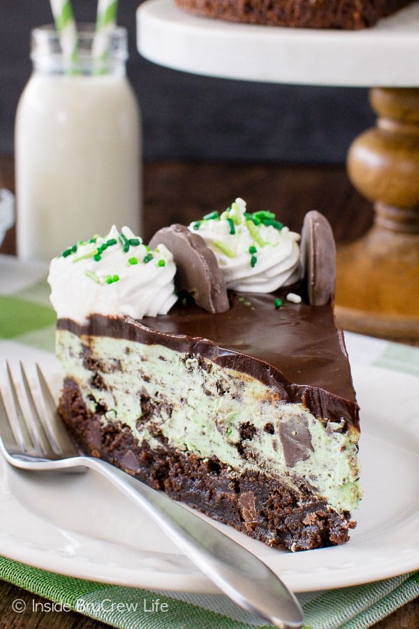 A slice of mint cheesecake with a brownie crust on a white plate.