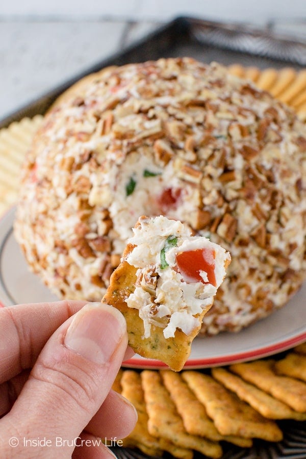 A cracker with cheese ball spread onto it with a large cheeseball in the background.