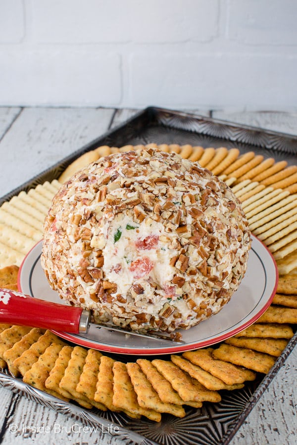 A cheese ball on a plate surrounded by an assortment of crackers.