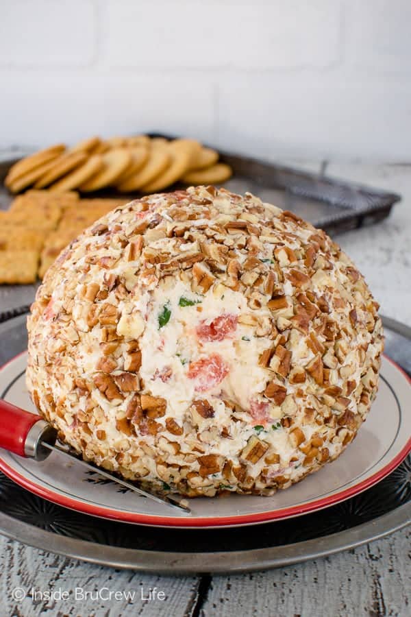 A homemade cheese ball covered in pecans on a white plate.