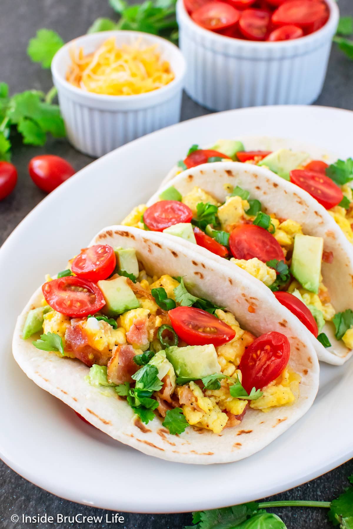 A plate filled with egg tacos with bacon and tomatoes.