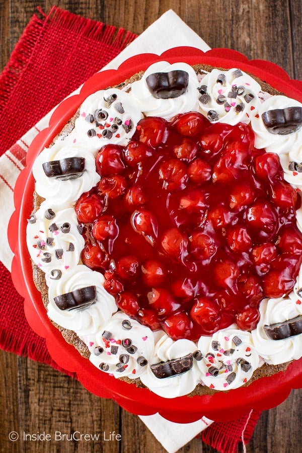 An overhead picture of a tart in a red pie pan topped with cool whip and cherry pie filling.