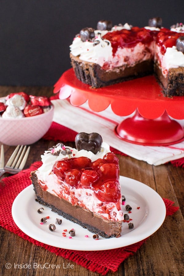 A white plate with a slice of chocolate tart with cream and cherry pie filling on top.