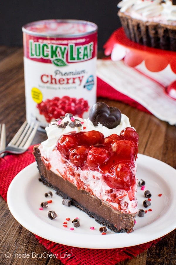 A white plate with a slice of chocolate tart with cream and cherry pie filling on top.