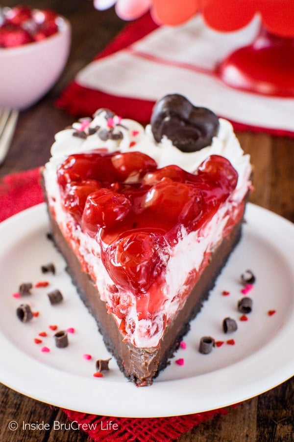 A front picture of a white plate with a slice of chocolate tart with cream and cherry pie filling on top.