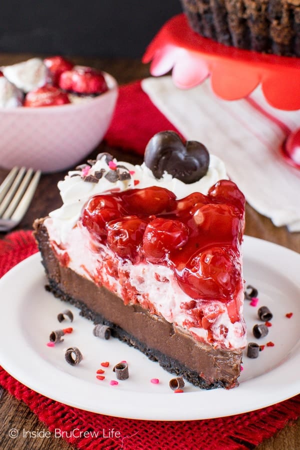 A white plate with a slice of chocolate tart with cream and cherry pie filling on top.