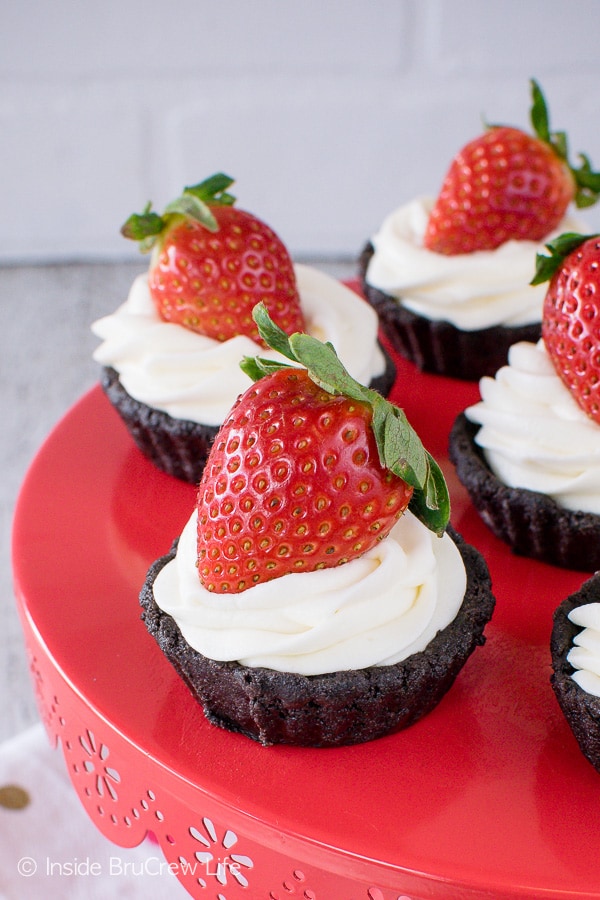A red cake plate with small chocolate tarts topped with cool whip and a strawberry.