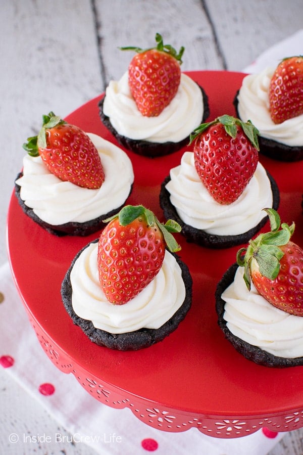 A red cake plate with small chocolate tarts topped with cool whip and a strawberry.