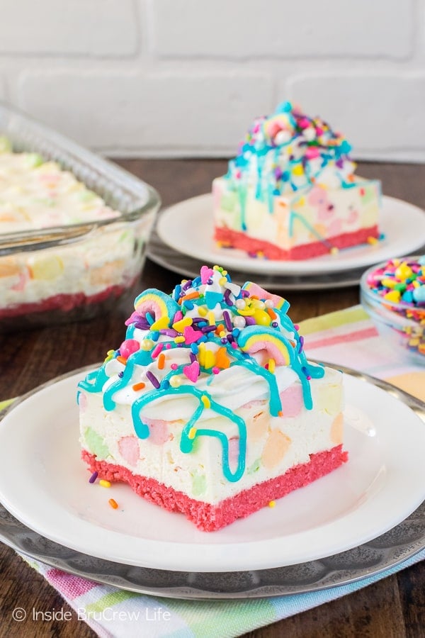 A white no bake cheesecake loaded with colorful marshmallows, brightly colored sprinkles, and a blue syrup drizzle.