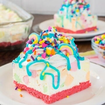 A white no bake cheesecake loaded with colorful marshmallows, brightly colored sprinkles, and a blue syrup drizzle.
