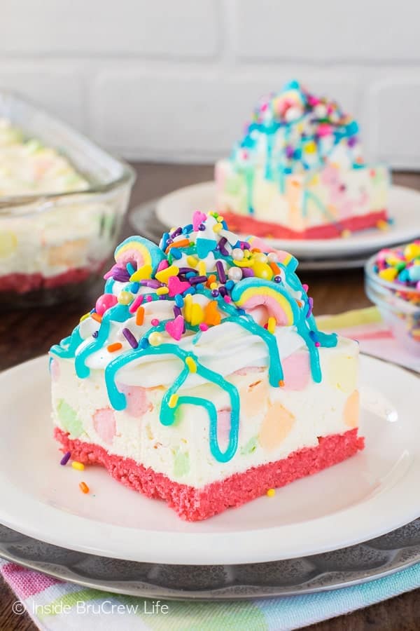 A white no bake cheesecake loaded with colorful marshmallows, brightly colored sprinkles, and a blue syrup drizzle.