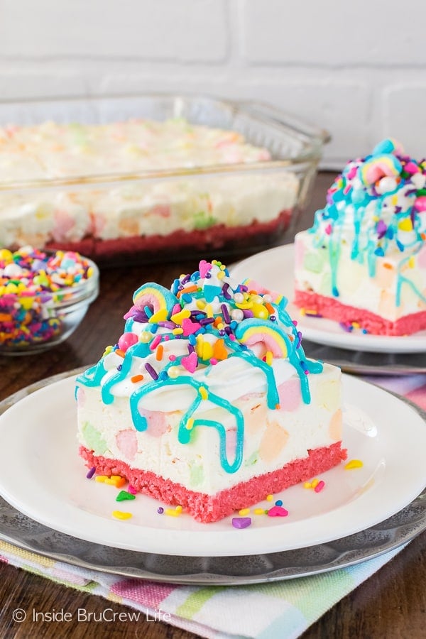 A white no bake cheesecake loaded with colorful marshmallows, brightly colored sprinkles, and a blue syrup drizzle.