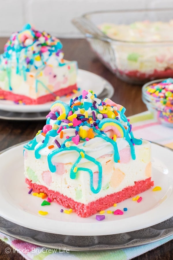 A white no bake cheesecake loaded with colorful marshmallows, brightly colored sprinkles, and a blue syrup drizzle.