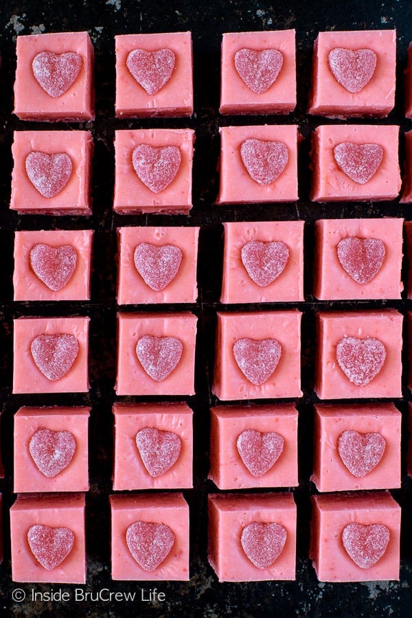 A cookie sheet loaded with squares of pink cinnamon fudge topped with a cinnamon jelly heart.