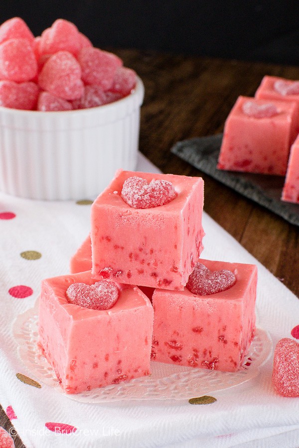 A white plate with squares of pink cinnamon fudge topped with a cinnamon jelly heart.