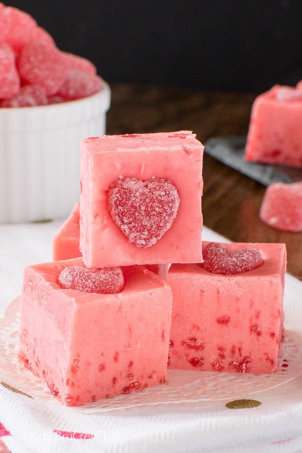 A white plate with squares of pink cinnamon fudge topped with a cinnamon jelly heart.