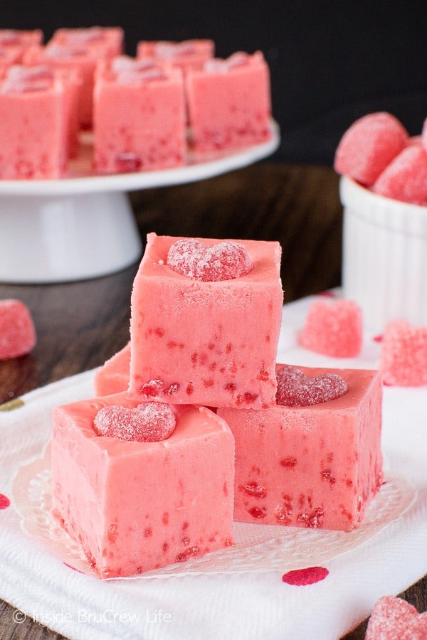 A white plate with squares of pink cinnamon fudge topped with a cinnamon jelly heart.