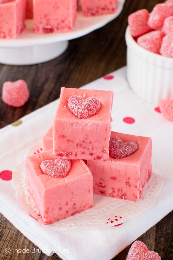 A white plate with squares of pink cinnamon fudge topped with a cinnamon jelly heart.