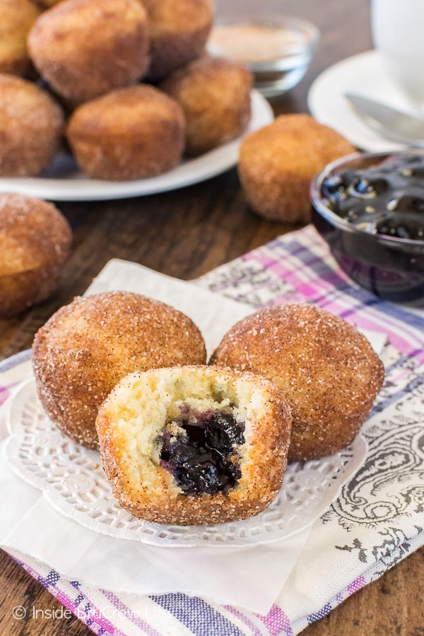 Three Blueberry Jelly Donut Holes on a white doily with a bite out of the front donut