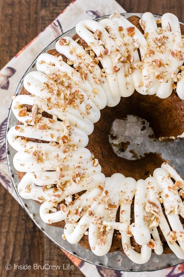An overhead picture of a carrot bundt cake topped with a white frosting and pecans on a metal cake plate.