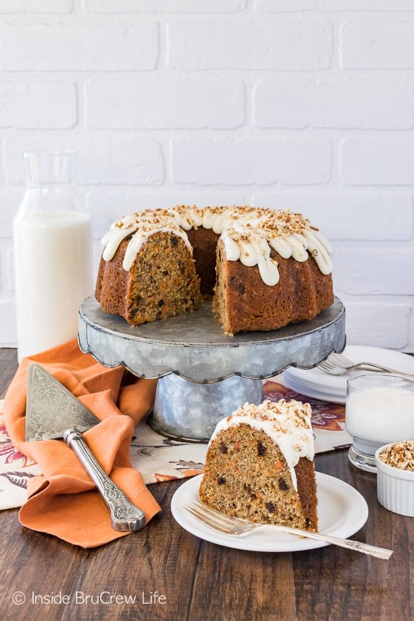 A slice of carrot bundt cake filled with raisins, spices, and carrots topped with a white frosting and pecans on a white plate.