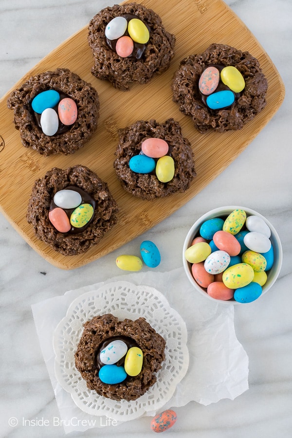 Chocolate bird nests with 3 malt chocolate eggs in them on a wooden cutting board.