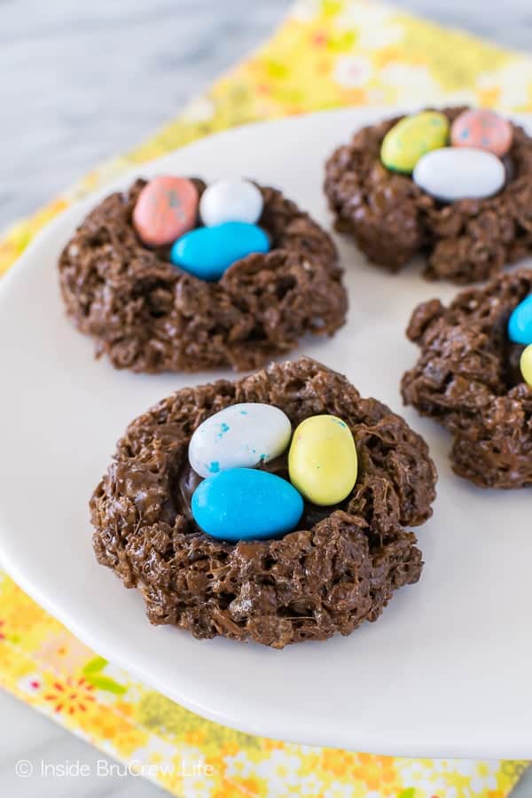 Edible chocolate bird nests with 3 colorful chocolate eggs in them on a white plate.