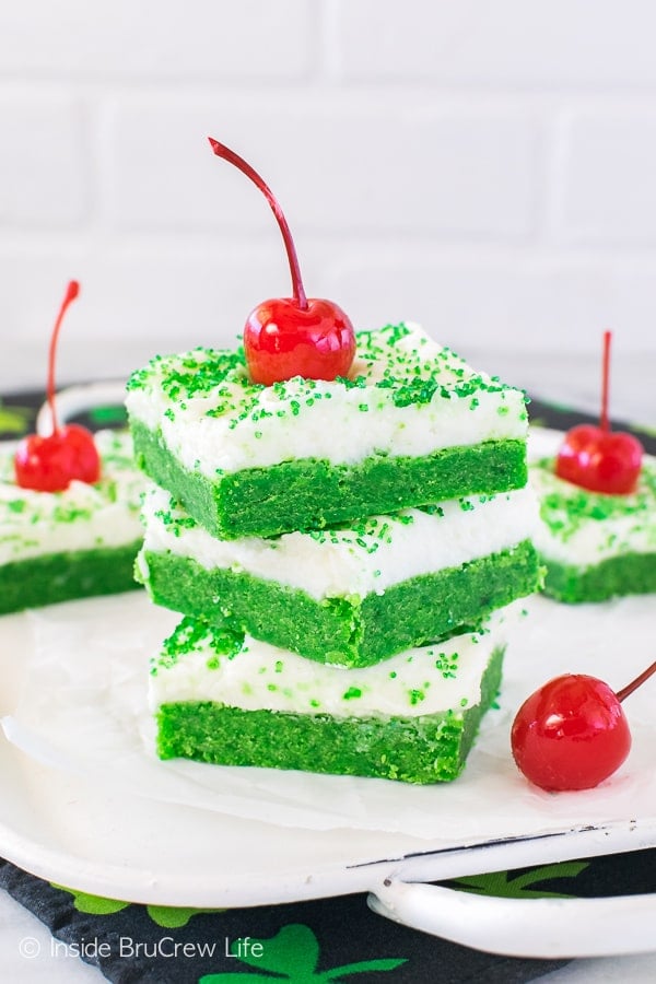 Three frosted shamrock shake sugar cookie bars stacked on top of each other with a cherry on top