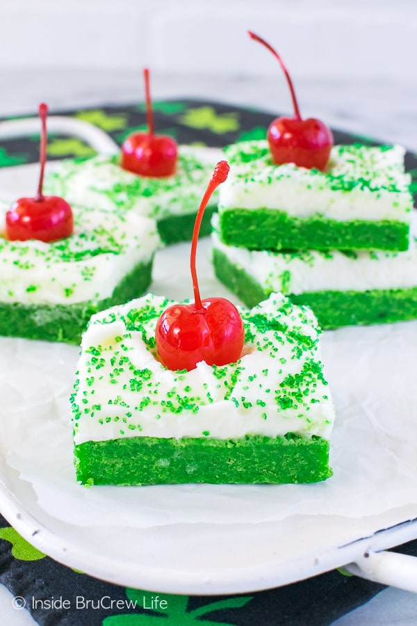 A white tray with squares of frosted Shamrock Shake Sugar Cookie Bars topped with green sugar and maraschino cherries