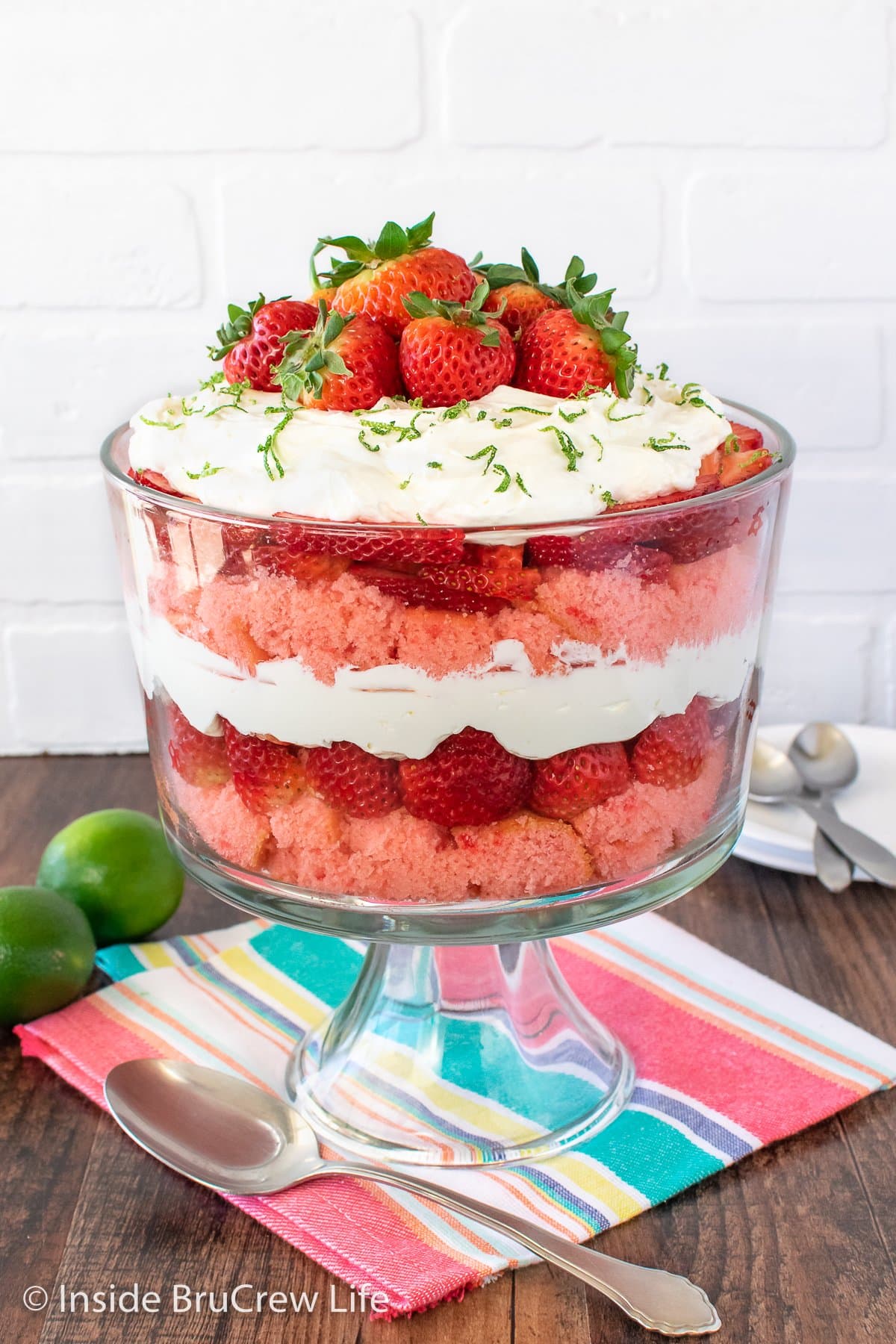 A trifle bowl filled with strawberry cake, cheesecake filling, and berries.