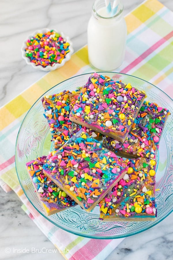 A blue plate with a stack of unicorn bars topped with vanilla frosting and lots of sprinkles on it