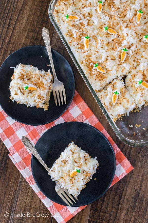 A piece of carrot cake with white frosting topped with toasted coconut on a black plate.