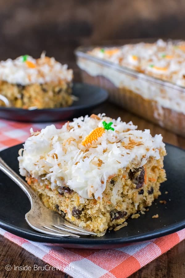A piece of carrot cake with white frosting topped with toasted coconut on a black plate.
