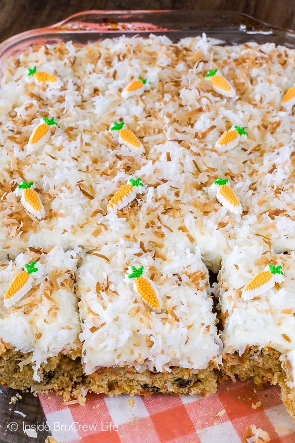 A clear pan full of carrot cake with white frosting topped with toasted coconut and candy carrots