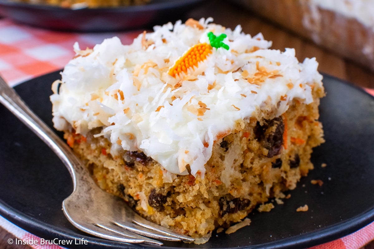 A frosted slice of spiced carrot cake on a black plate.