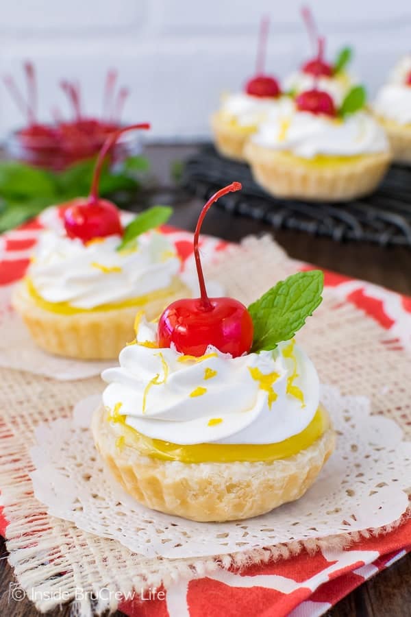 Mini lemon cheesecake pies topped with cherries on a white doily.