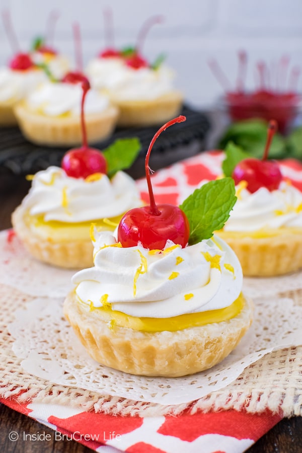 Mini lemon cheesecake pies topped with cherries on a white doily.