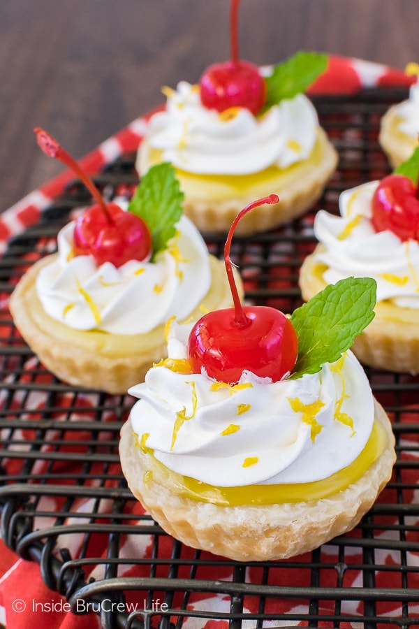 Mini lemon cheesecake pies topped with cherries on a black cooling rack.