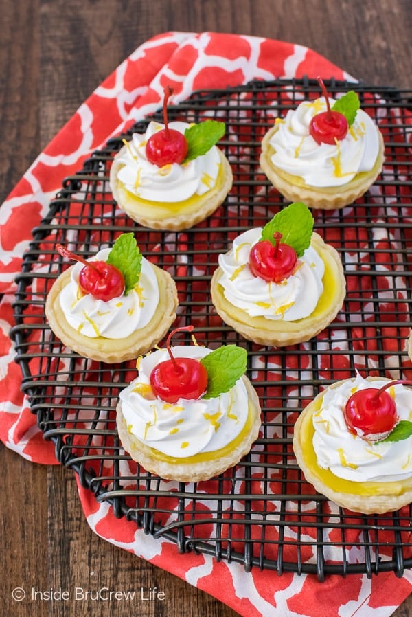 Mini lemon cheesecake pies topped with cherries on a black cooling rack.