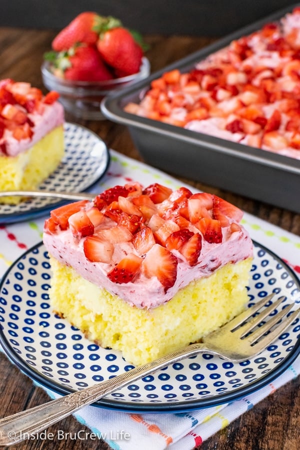 A blue and white plate with a square of lemon strawberry cake topped with fresh strawberries on it.