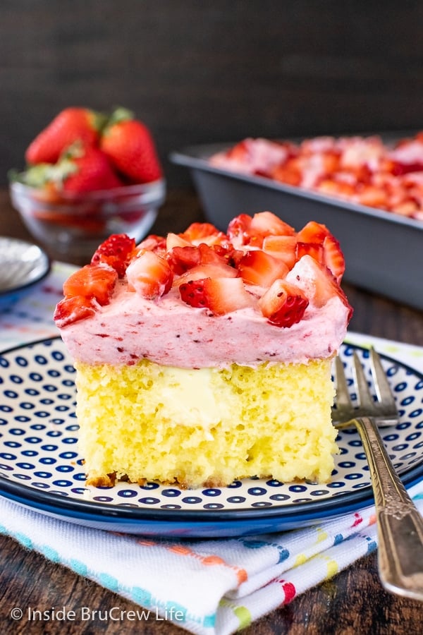 A square of lemon poke cake topped with strawberry mousse and fresh strawberries on a blue and white plate.