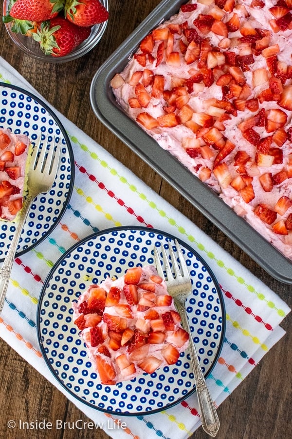 Overhead picture of blue and white plates with squares of lemon poke cake topped with strawberry mousse and fresh strawberries.