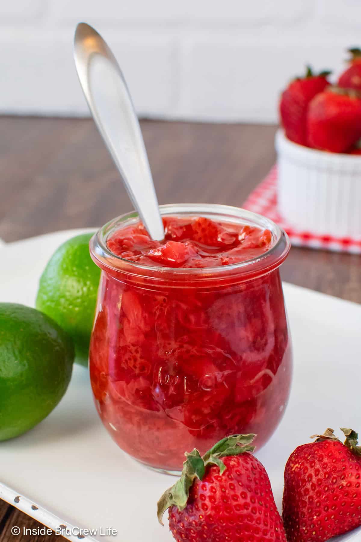 A clear jar of easy strawberry sauce with a spoon in it.