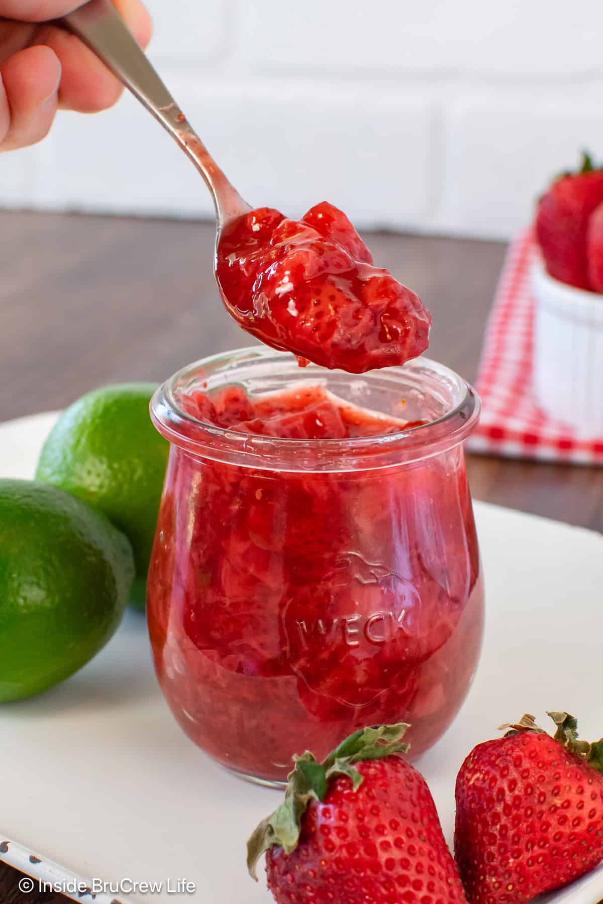 A jar of strawberry sauce with a spoonful being lifted out of it.
