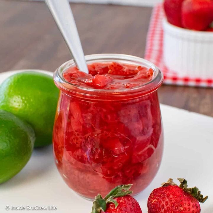 A clear jar of easy strawberry sauce with a spoon in it.