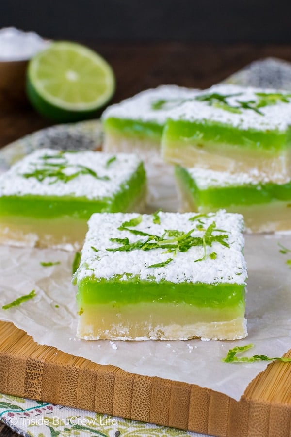 A wooden cutting board with shortbread bars topped with key lime filling stacked on it.