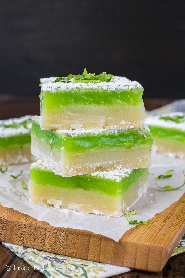 A wooden cutting board with three shortbread bars made with key lime filling stacked on it.